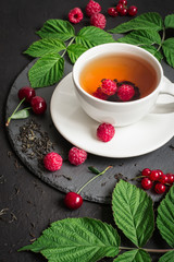 cup of Berry tea and ripe raspberry, cherry, currant on a black background