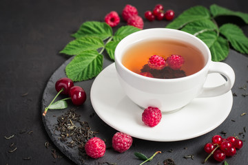 Berry tea and ripe raspberry, cherry, currant on a black background