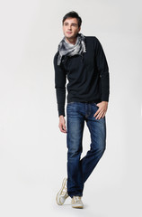Studio picture of a young and handsome man in jeans with scarf posing