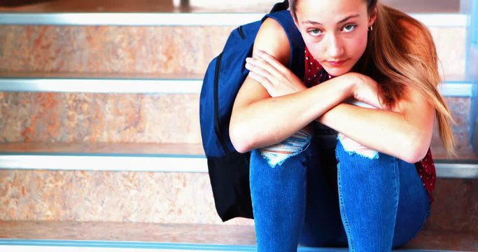 Sad schoolgirl sitting alone on staircase