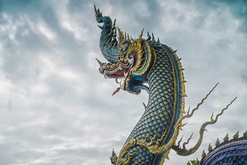 Fototapeta na wymiar Naga Head Statue / Chiang Rai, Thailand - July 12, 2017: Naga Head Statue Inside Wat Rong Sua Ten Or Blue Temple At Rain Clouds Background.