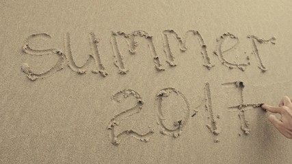 SUMMER 2017 written on the beach sand washed aways by waves.
