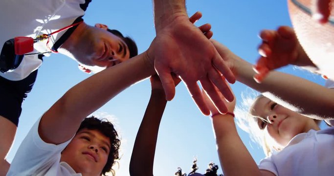 School kids and coach stacking hands in campus