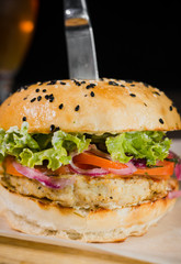 Burger with fried potatoes and tomato sauce on a wooden stand with a glass of beer
