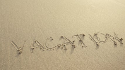 VACATION written on the beach sand washed aways by waves.