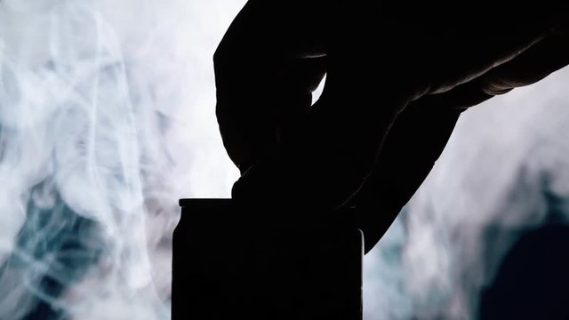 A smokey silhouette close-up shot of hands opening an aluminium can.
