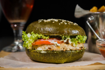 Green burger with fried potatoes and tomato sauce on a wooden stand with a glass of beer