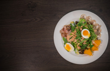 Salad with egg and mushrooms on a white plate and a wooden background