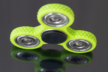 A green hand spinner or fidget spinner on dark mirror surface. A toy for stress relieving. Close...