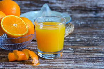 Glass of freshly squeezed orange juice,  oranges fruit cut in half and glass citrus juicer on wooden table.Copy space.