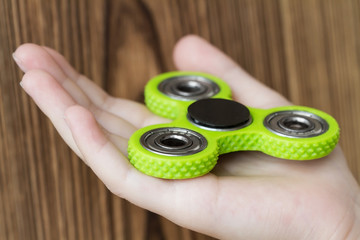 A green hand spinner or fidget spinner on the girl's hand on the wooden background. A toy for...
