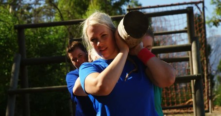 Group of fit women carrying a heavy wooden log during obstacle course - Powered by Adobe