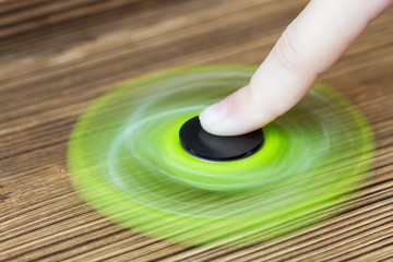 Fototapeta na wymiar A green hand spinner or fidget spinner on the wooden background. A toy for stress relieving. Close up. Selective focus.