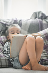 little girl reading book on sofa
