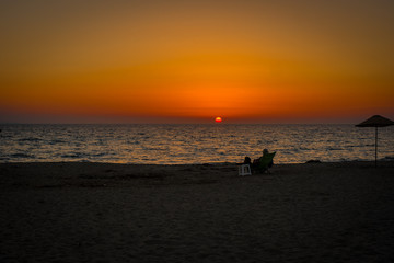 Naklejka na ściany i meble man sitting alone on the beach sunset