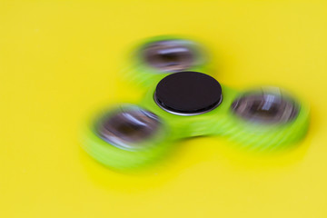 A green hand spinner or fidget spinner is rotating on the yellow background. A toy for stress...