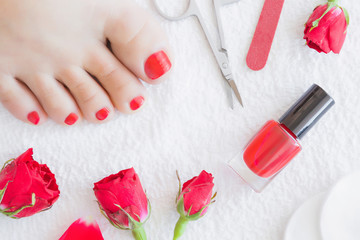 Obraz na płótnie Canvas Cares about woman's foot nails. Pedicure beauty salon. Scissors, nail file, red nail polish and red roses on the white towel background.