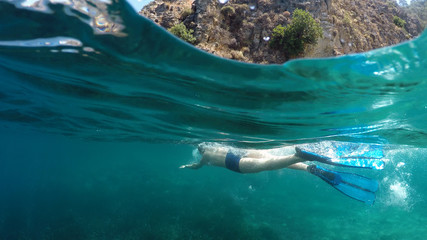 Half underwater close up, swimmer in flippers dives into the sea