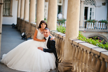 Elegant and gentle bride sitting on her husband's knees. Fantastic background with ancient...