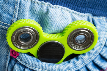 Green fidget spinner in the child's jeans pocket for playing with friends. Closeup. Selective focus.