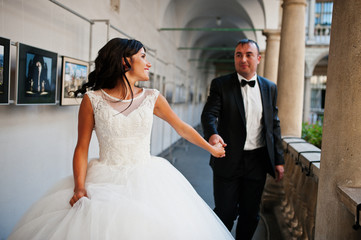 Amazing young attractive newly married couple walking and posing in the downtown with beautiful and ancient architecture on the background on their wedding day.