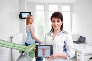 Obraz na płótnie Canvas Beautiful happy female doctor gynecologist smiling to the camera holding digital tablet with a picture of uterus her patient on the background copyspace gynecology mammography feminine health.