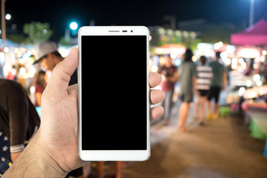 Man's hand holding smartphone and blurred image of street market at night.