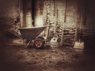 Obraz premium Schubkarre und Gartenwerkzeuge stehen vor einem alten Bauernhaus