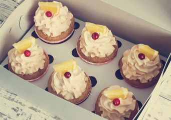 Vanilla cupcakes with a cap of cream on white wooden tablein the box