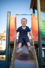 Fototapeta premium Happy boy riding from childrens slides