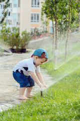 Little cheerful child playing in the garden with automatic watering lawns