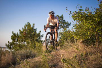 Fototapeta premium Bicycle rider on professional cyclocross bike ride downhill, pine and lake background 
