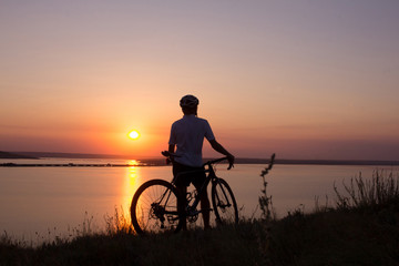 silhouette of a cyclist  watching sunset in lake, male bicycle rider in helmet during sunset 