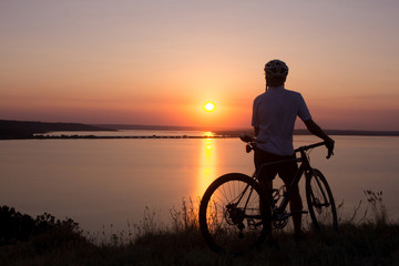 Fototapeta na wymiar silhouette of a cyclist watching sunset in lake, male bicycle rider in helmet during sunset 