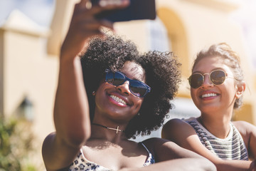 Two happy female friends taking selfie by smartphone - obrazy, fototapety, plakaty