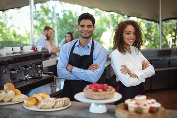 Portrait of smiling waiter and waitress standing with arms crossed at counter