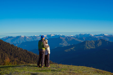 Couple of travelers, hugging, is admiring the dawn in the mountains