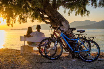 A couple of lovers watching the sunset sitting on a bench by the sea.