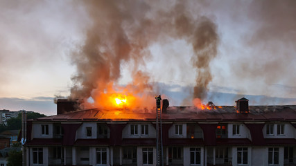 Burning fire flame with smoke on the apartment house roof in the city, firefighter on the ladder...