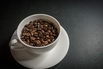 Roasted coffee beans in white cup on dark background. Selective focus.