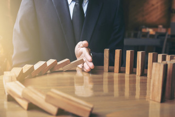 Close up of businessman hand Stopping Falling wooden Dominoes effect from continuous toppled or...