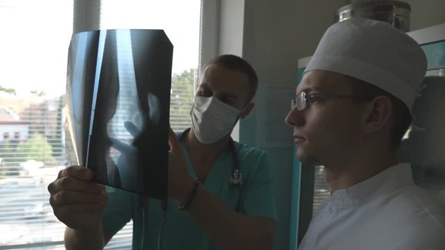 Two caucasian doctors view mri picture and discussing about it. Medical workers in hospital examine x-ray prints. Male medics consult with each other while looking at x ray image. Close up Slow motion