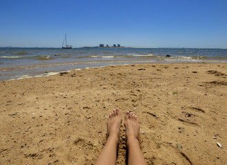 Womans legs at a beach with shallow waters in Setubal, Portugal - Troia peninsula in the background
