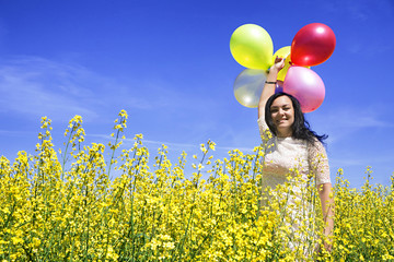 Woman holding colorful balloons in mustard field on a sunny day