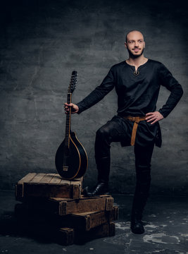 Studio image of male musicians in old traditional Celtic clothes holds vintage mandolin.
