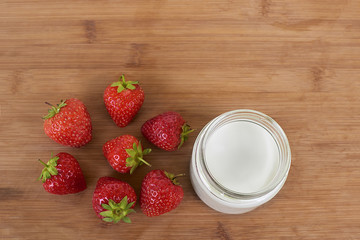 Goat milk yogurt in glass jar and strawberries on a wood background from the top