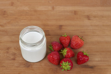 Yogurt in glass jar and strawberries on a wood background - from the top