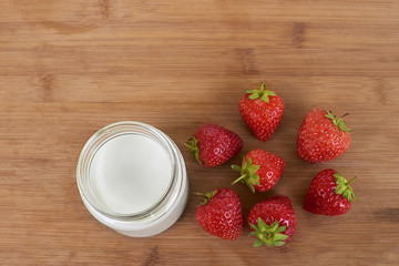Yogurt in glass jar and strawberries on a wood background - directly from the top