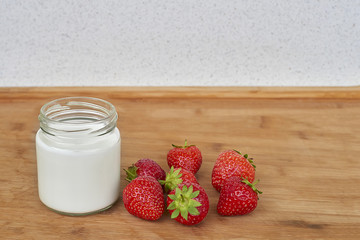 Yogurt in glass jar and strawberries on a wood background - horizontal