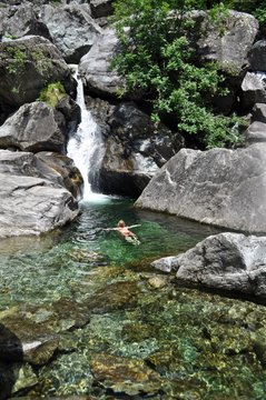 Frau schwimmt im Wasserbecken vom Bach unterhalb von einem Wasserfall im Tessin, Schweiz